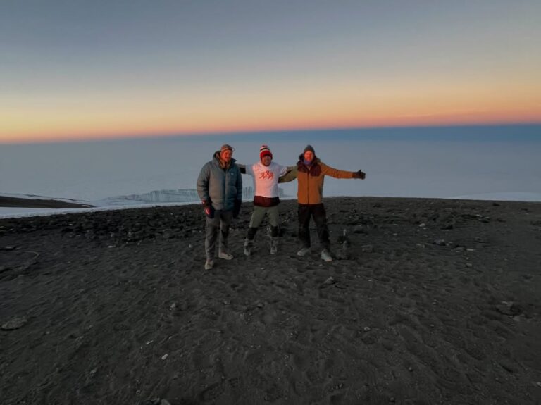Three Kilimanjaro trekkers above the clouds near the summit glaciers at dawn