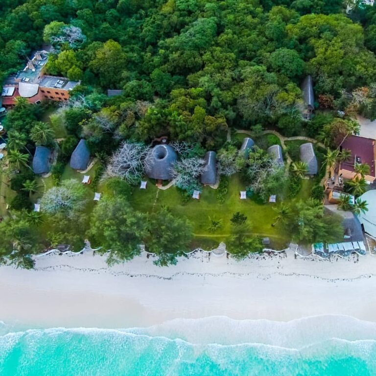 Aerial view of a green coastal retreat beside a white-sand beach