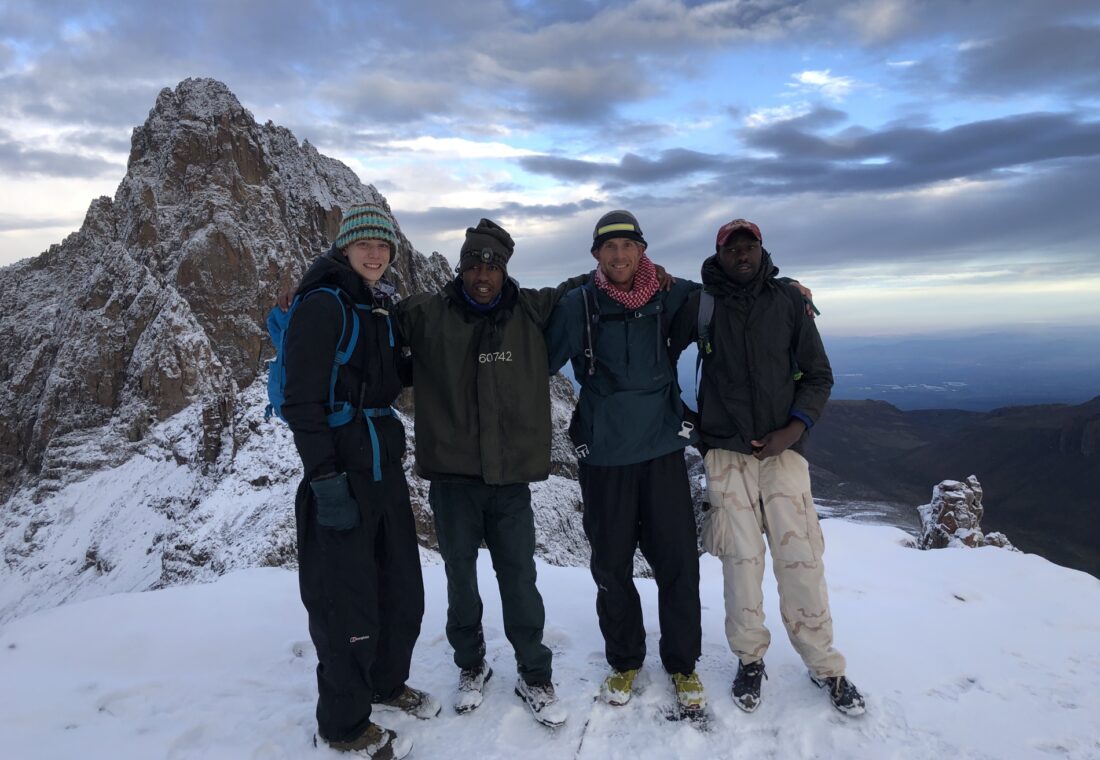 Joseph Kimani and the Mount Kenya team standing together in snow beside the mountain peaks