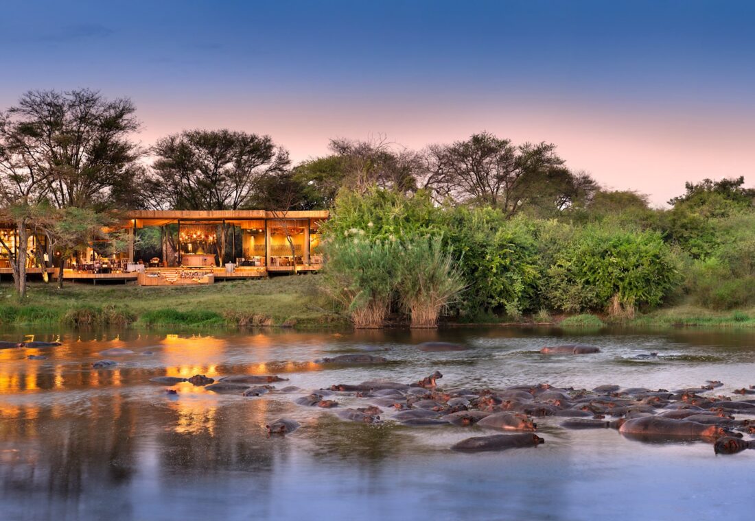 Grumeti Serengeti River Lodge beside a hippo-filled river at dusk