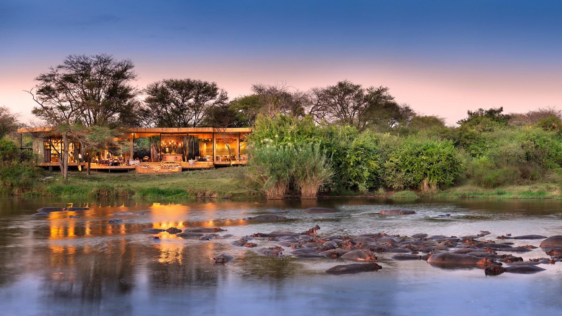 Grumeti Serengeti River Lodge beside a hippo-filled river at dusk