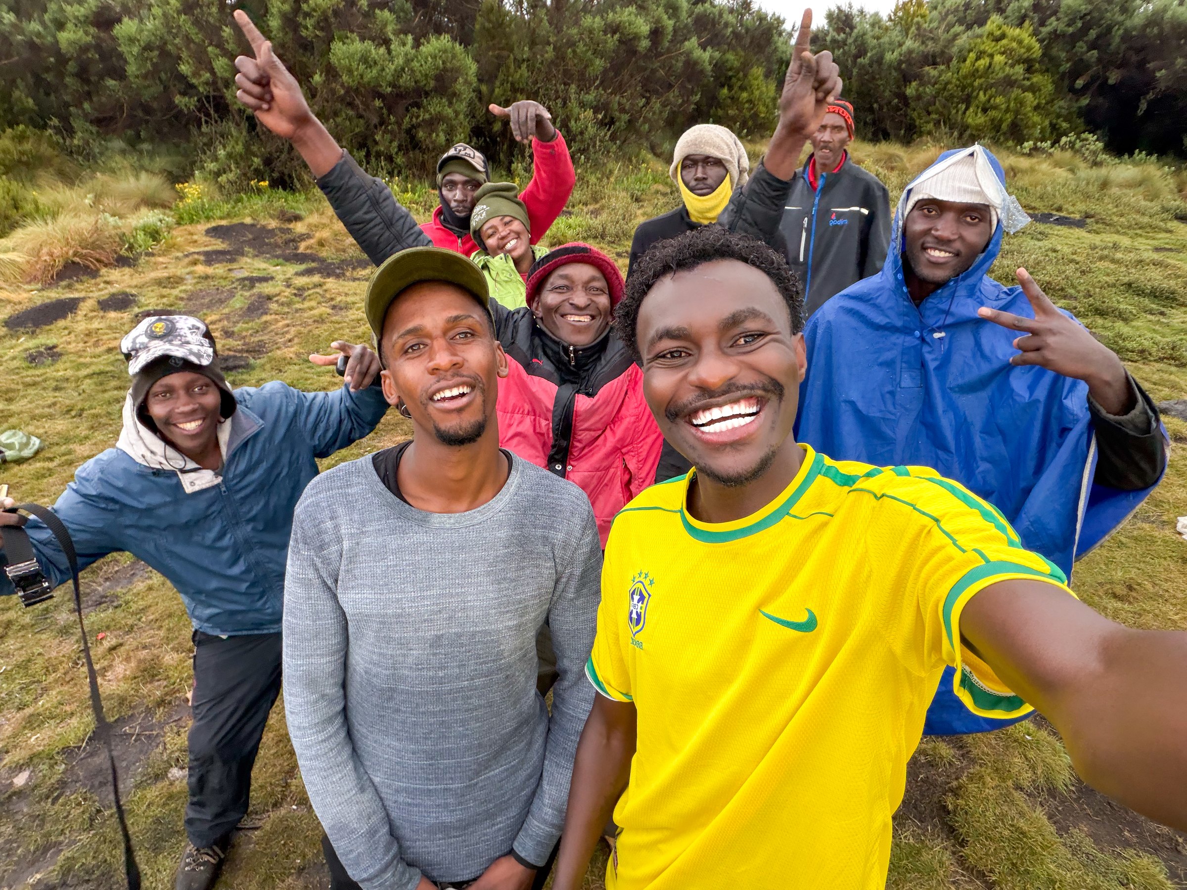 Nine people smiling for a group selfie among highland vegetation on Mount Kenya