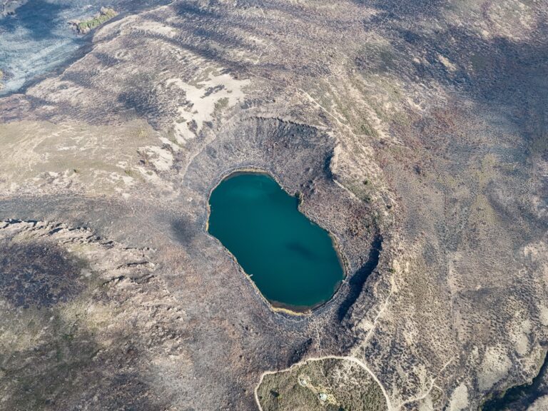 Aerial view of Lake Rutundu enclosed by moorland slopes, with the log cabins below, on Mount Kenya